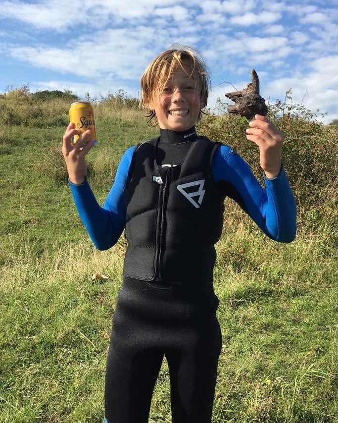 Young Noah in a wetsuit and impact vest, laughing on the grass after a day on the water