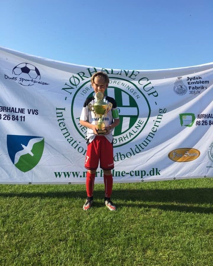 Noah as a boy in his football kit, holding a trophy after a tournament