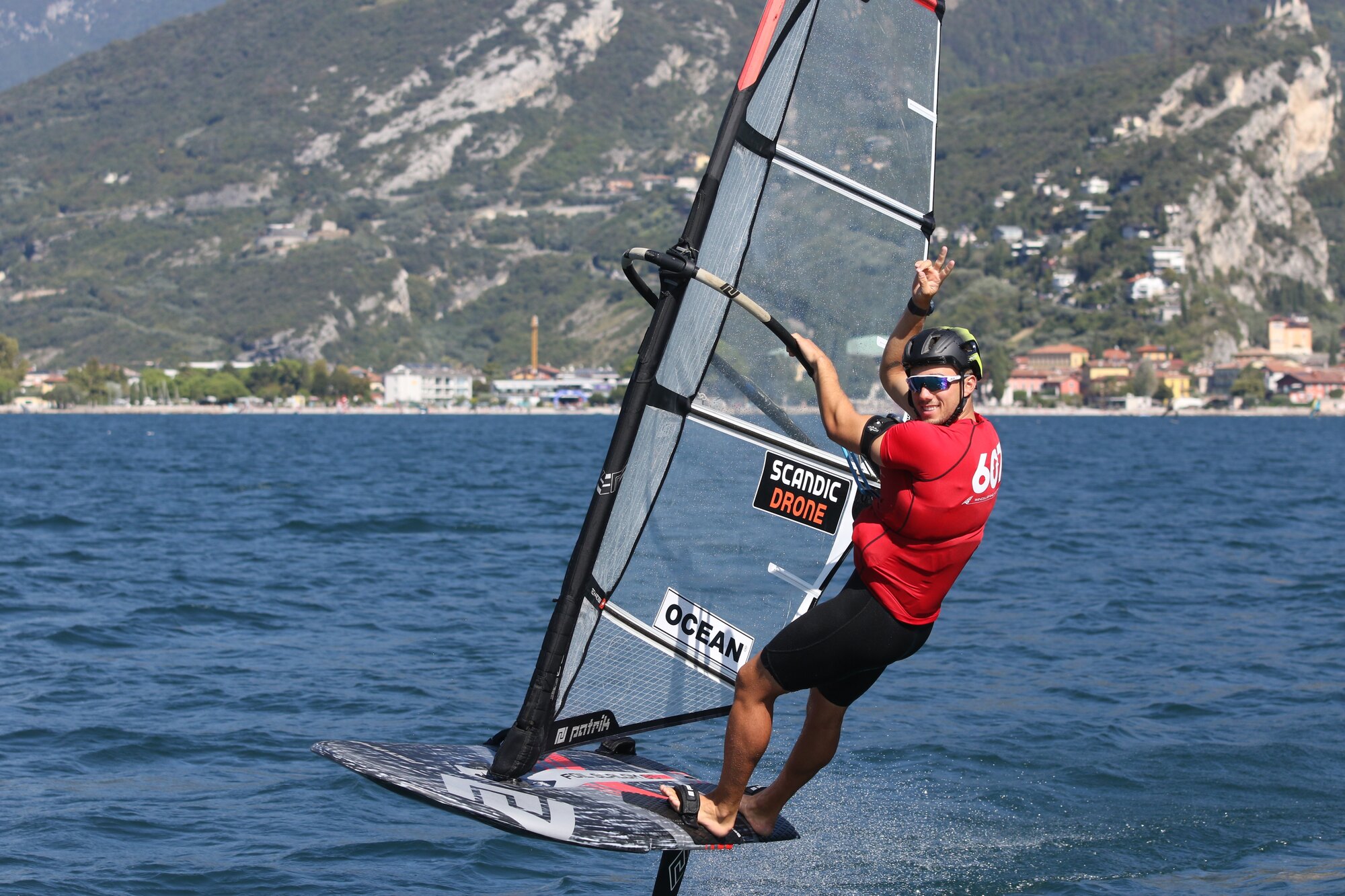 Noah in a red race jersey foiling on Lake Garda, mountains behind